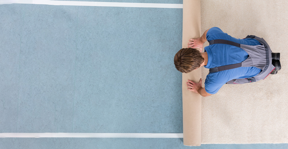 Carpet Installer - an image of a carpet installer rolling out carpet over underpad